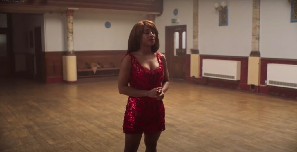 A woman in a red dress stands in the center of the room