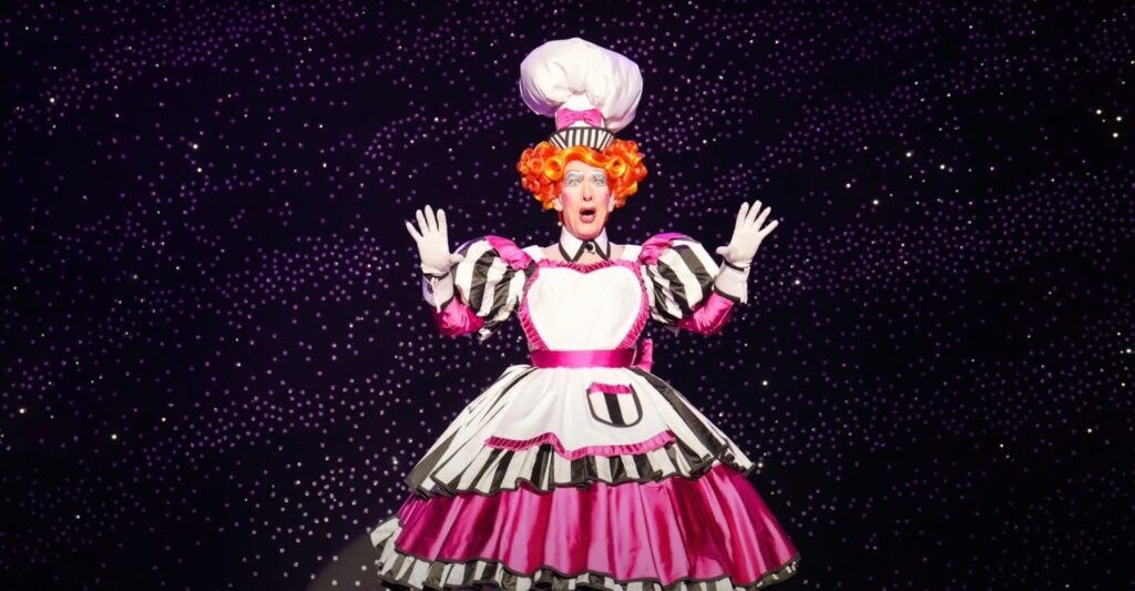 A woman in a bright costume with red hair performs on stage