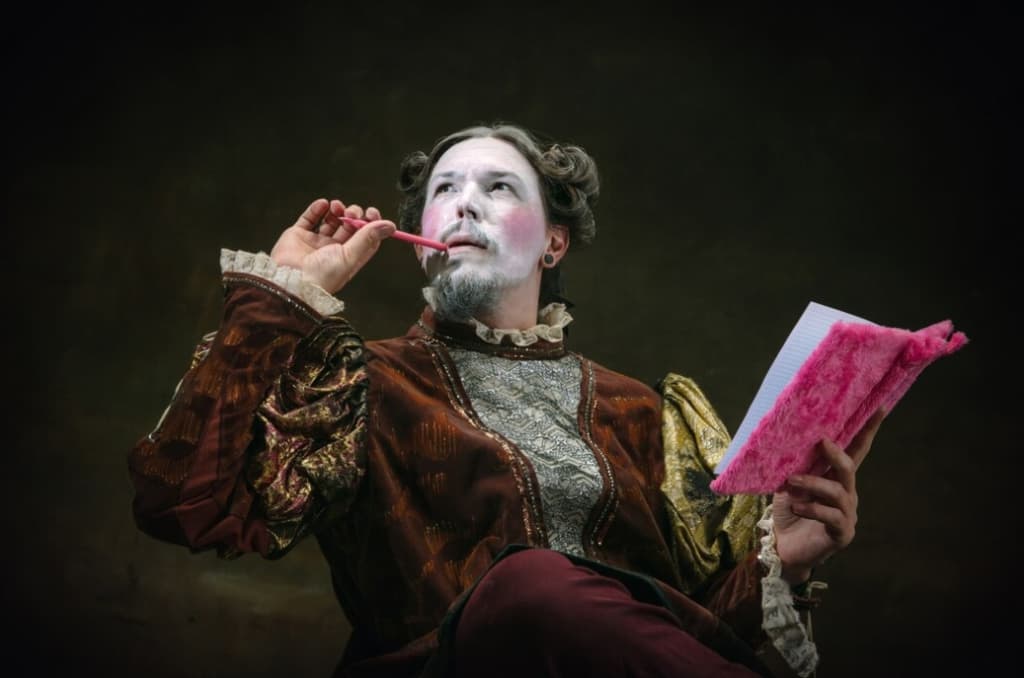 Man in historical attire uses a pink pen near mouth and holds a pink fluffy notebook