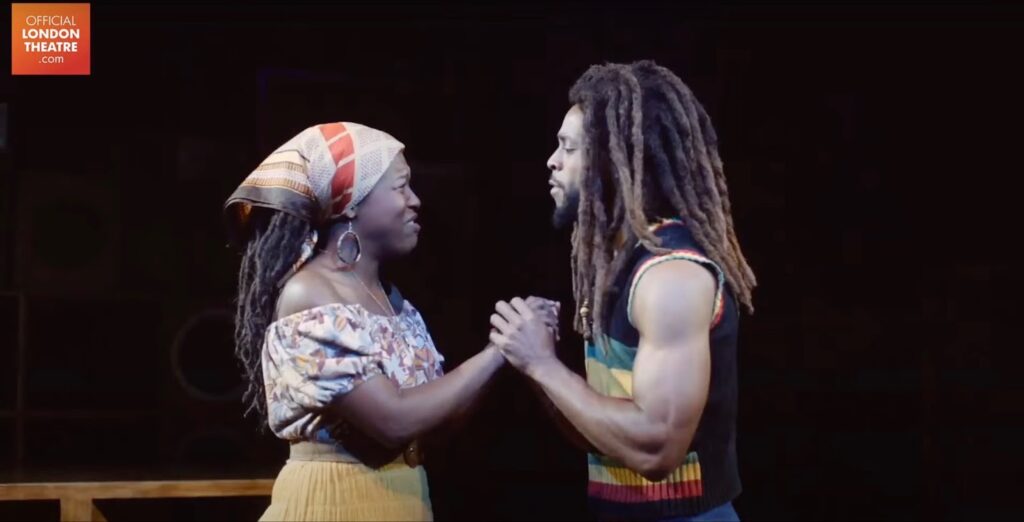 An artist dressed as Bob Marley plays a role with a woman on stage