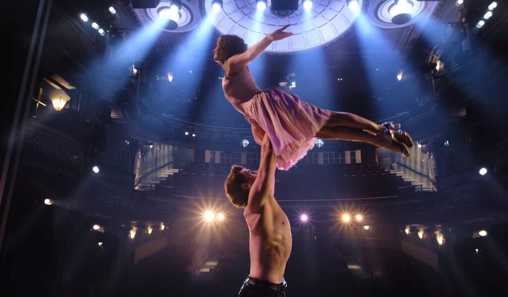 A dancer held aloft in a grand, well-lit theater