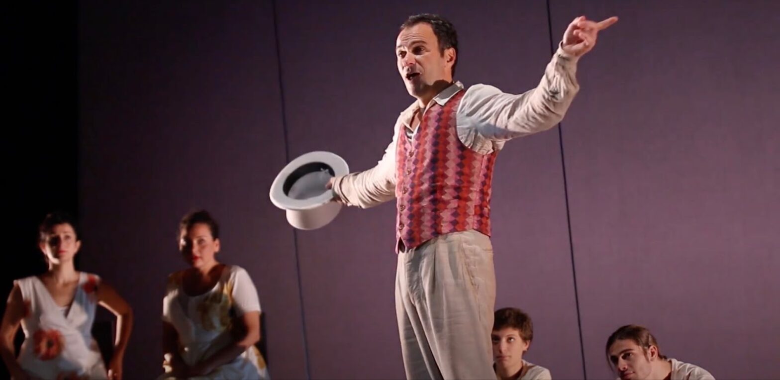 A man with a top hat in his hands plays in the theater