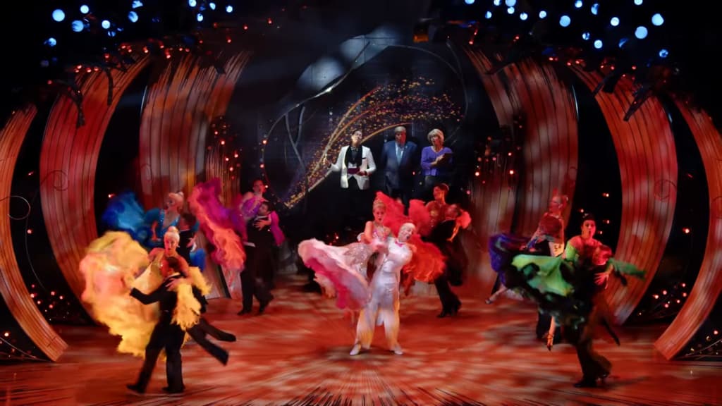 Dancers in vivid attire twirl on stage, with three central figures observing amid cascading gold lights