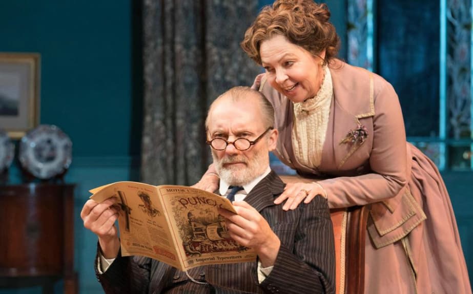 An elderly man reading a vintage newspaper with a smiling woman leaning over his shoulder in a historical setting